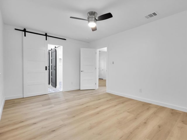 unfurnished room with a barn door, ceiling fan, and light hardwood / wood-style floors