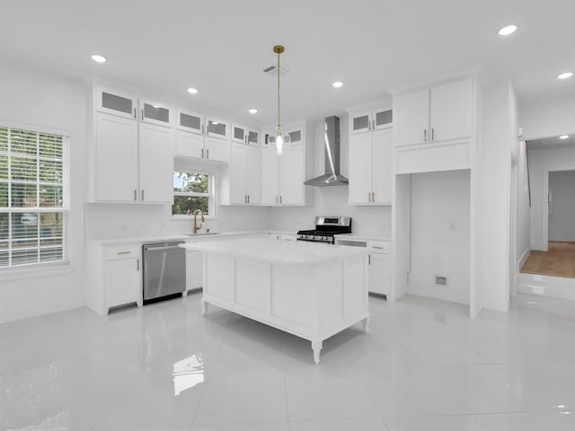 kitchen featuring a center island, wall chimney exhaust hood, stainless steel appliances, pendant lighting, and white cabinets