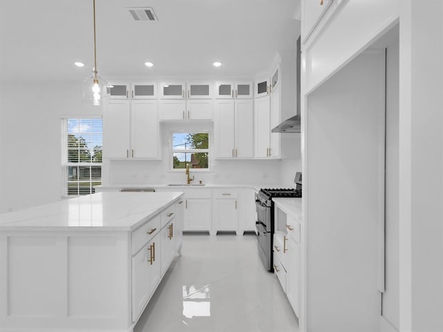 kitchen featuring light stone countertops, white cabinetry, range with two ovens, and a kitchen island