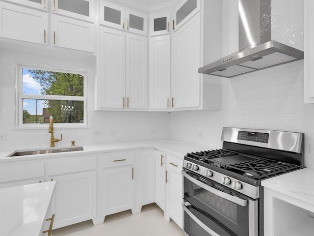 kitchen featuring light stone counters, sink, wall chimney range hood, range with two ovens, and white cabinetry