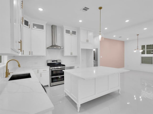 kitchen featuring a center island, double oven range, sink, wall chimney exhaust hood, and white cabinetry