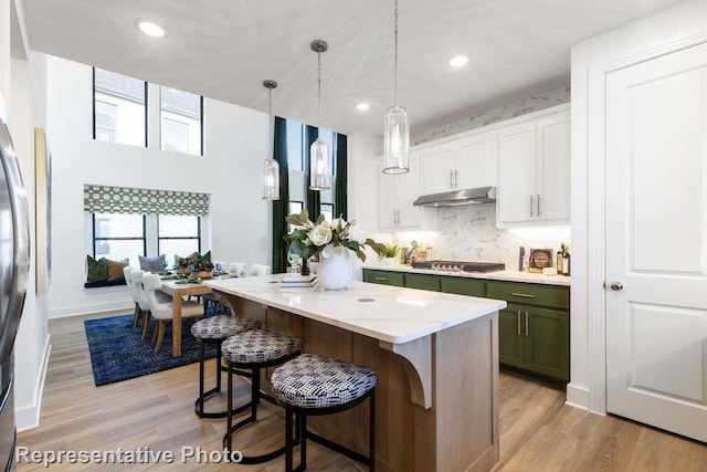 kitchen featuring light wood-type flooring, decorative light fixtures, a center island, white cabinetry, and stainless steel gas stovetop