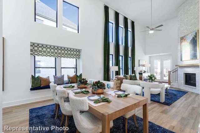 dining space with a high ceiling, french doors, a brick fireplace, hardwood / wood-style flooring, and ceiling fan