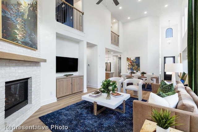 living room with ceiling fan, light hardwood / wood-style floors, a fireplace, and a high ceiling