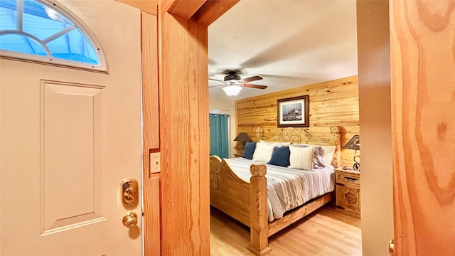 bedroom with ceiling fan, wood walls, and light wood-type flooring