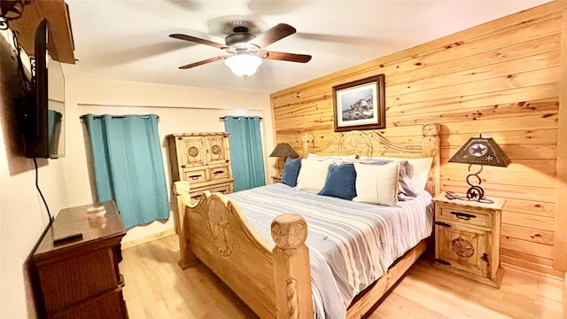 bedroom with wood walls, ceiling fan, and light hardwood / wood-style floors