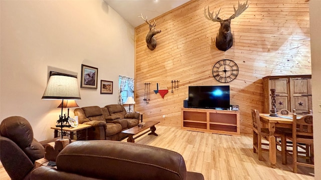 living room featuring wood walls, a towering ceiling, and light hardwood / wood-style flooring