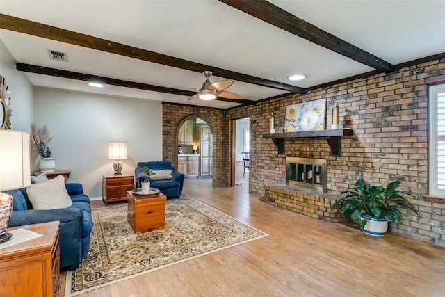 living room with a wealth of natural light, light hardwood / wood-style flooring, brick wall, and a brick fireplace