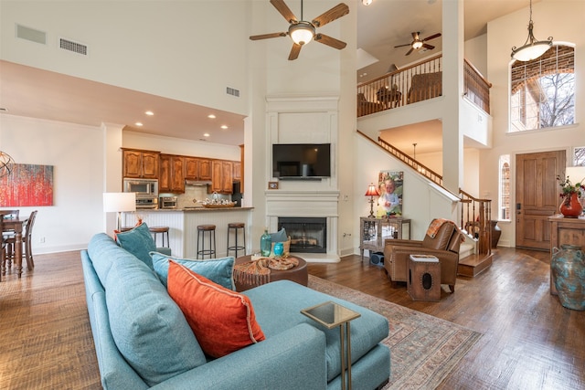 living area featuring a large fireplace, baseboards, visible vents, dark wood finished floors, and stairs