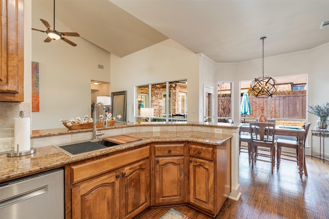 kitchen featuring a peninsula, a sink, hanging light fixtures, stainless steel dishwasher, and brown cabinetry