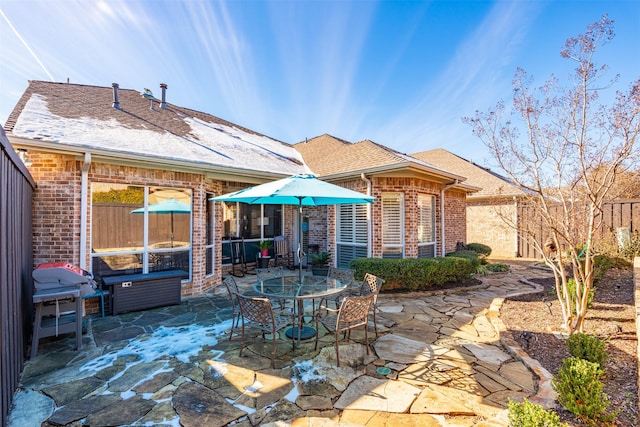 rear view of property with brick siding, a patio, fence, and roof with shingles