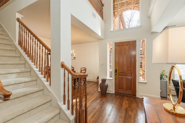 entrance foyer with a high ceiling, visible vents, stairs, ornamental molding, and dark wood-style floors