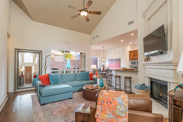 living area with high vaulted ceiling, a fireplace, wood finished floors, visible vents, and a ceiling fan