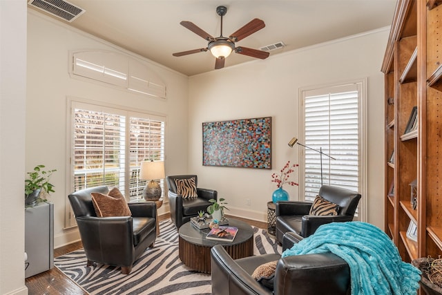 living area featuring baseboards, ceiling fan, visible vents, and crown molding