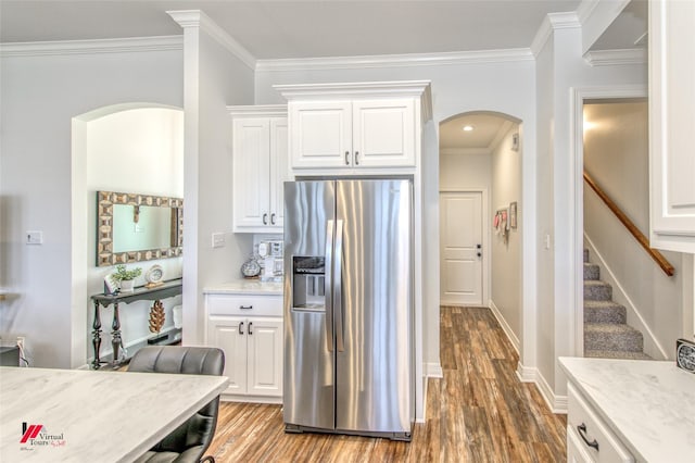 kitchen with light hardwood / wood-style flooring, stainless steel fridge with ice dispenser, ornamental molding, light stone counters, and white cabinetry