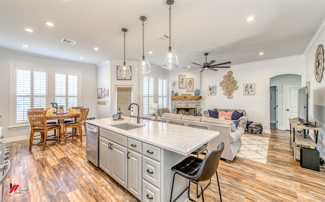 kitchen with light stone counters, stainless steel dishwasher, ceiling fan, a kitchen island with sink, and sink