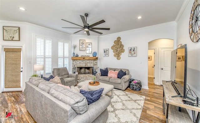 living room with a brick fireplace, light hardwood / wood-style flooring, ceiling fan, and ornamental molding