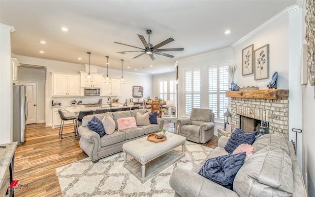 living room with a fireplace, light wood-type flooring, ceiling fan, and crown molding