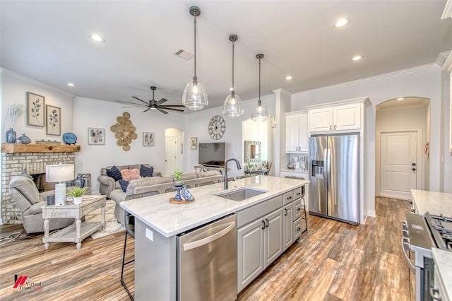 kitchen with stainless steel appliances, ceiling fan, sink, a center island with sink, and white cabinets