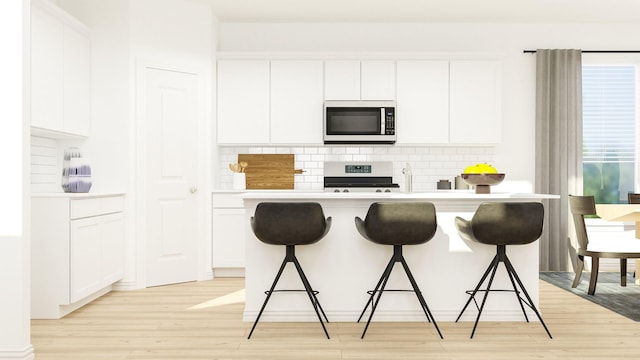 kitchen with white cabinets, appliances with stainless steel finishes, light hardwood / wood-style floors, and a kitchen breakfast bar