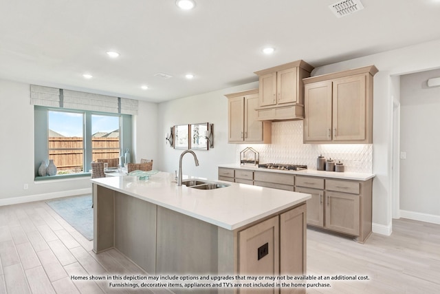 kitchen with sink, stainless steel gas cooktop, light brown cabinetry, a center island with sink, and light wood-type flooring