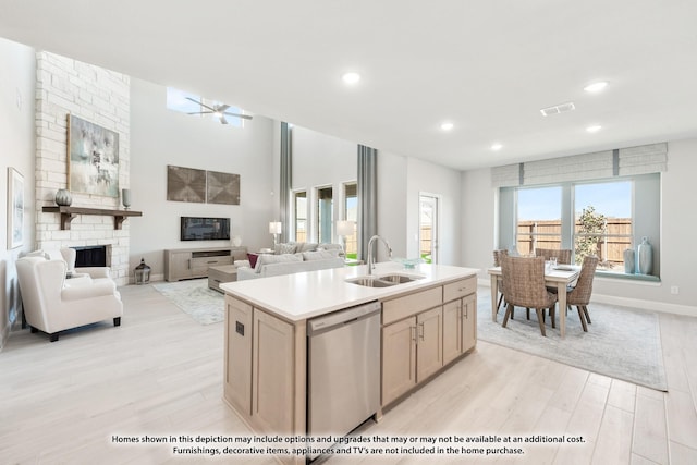 kitchen with stainless steel dishwasher, a large fireplace, sink, a center island with sink, and light hardwood / wood-style floors