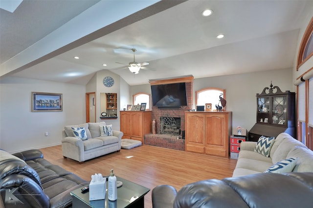 living room featuring a brick fireplace, vaulted ceiling, light hardwood / wood-style flooring, and ceiling fan