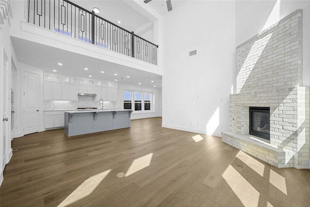 unfurnished living room featuring wood finished floors, visible vents, a towering ceiling, and a ceiling fan