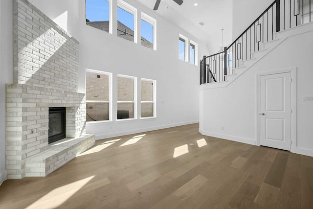 unfurnished living room featuring a ceiling fan, wood finished floors, baseboards, a high ceiling, and a brick fireplace