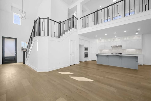 unfurnished living room featuring a chandelier, a high ceiling, light wood-style floors, and stairway