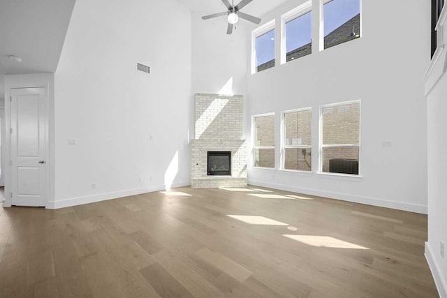 unfurnished living room featuring wood finished floors, a towering ceiling, a fireplace, baseboards, and visible vents