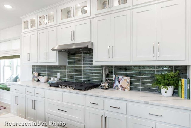 kitchen featuring light stone counters, stainless steel gas stovetop, backsplash, and white cabinetry