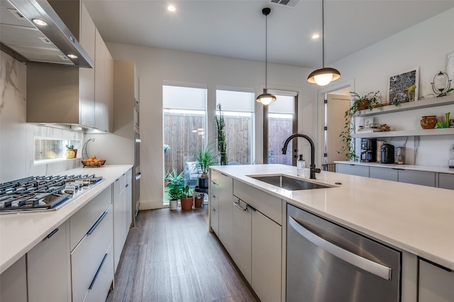 kitchen with stainless steel appliances, hanging light fixtures, wall chimney range hood, white cabinets, and sink