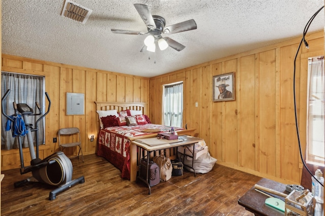 bedroom with ceiling fan, dark hardwood / wood-style flooring, electric panel, wood walls, and a textured ceiling