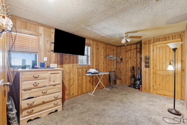 misc room featuring wooden walls, ceiling fan, light carpet, and a textured ceiling