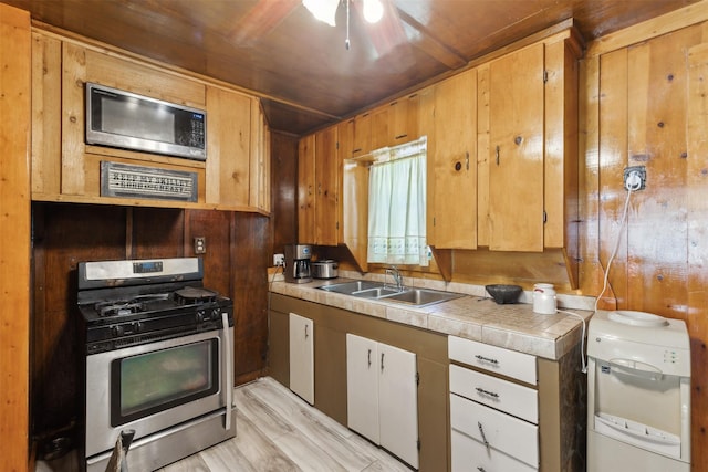 kitchen featuring stainless steel gas range, wooden walls, sink, light hardwood / wood-style flooring, and wooden ceiling