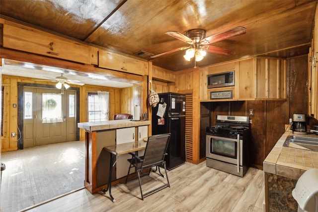 kitchen with built in microwave, tile counters, wooden ceiling, stainless steel range with gas cooktop, and black refrigerator