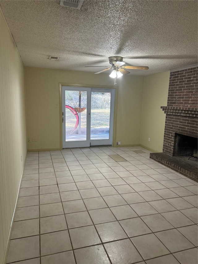 unfurnished living room featuring a brick fireplace, a textured ceiling, ceiling fan, wooden walls, and light tile patterned flooring