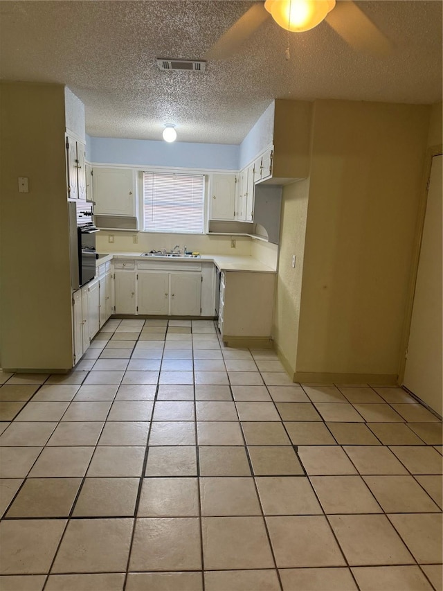 kitchen featuring light tile patterned floors, a textured ceiling, white cabinetry, and ceiling fan