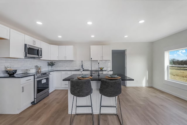 kitchen featuring backsplash, stainless steel appliances, white cabinets, a center island, and light hardwood / wood-style floors