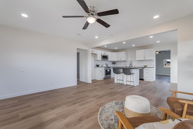 living room with ceiling fan, sink, and light wood-type flooring