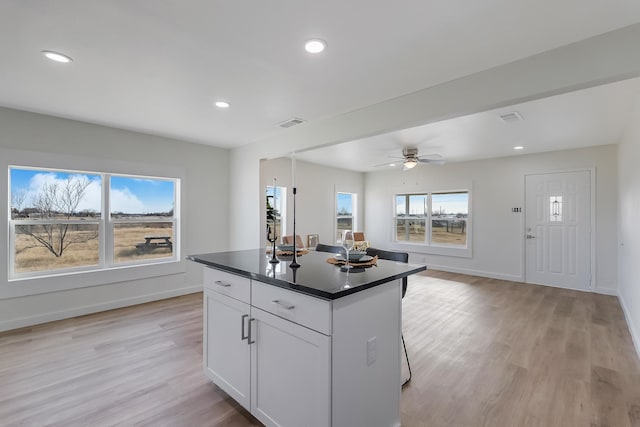 kitchen with a breakfast bar, ceiling fan, a kitchen island, light hardwood / wood-style floors, and white cabinetry