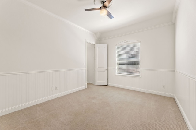 spare room with ceiling fan, crown molding, and light colored carpet