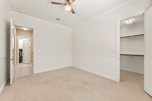 unfurnished bedroom featuring light carpet, crown molding, ceiling fan, a spacious closet, and a closet