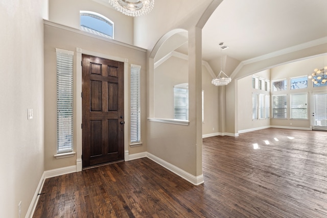 entryway featuring a chandelier, a towering ceiling, crown molding, and dark wood-type flooring