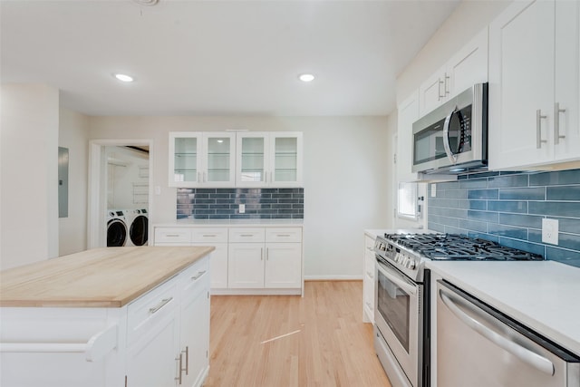 kitchen with light wood-type flooring, backsplash, stainless steel appliances, washing machine and clothes dryer, and white cabinets