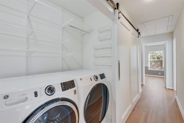 clothes washing area featuring a barn door, washer and dryer, and light hardwood / wood-style floors