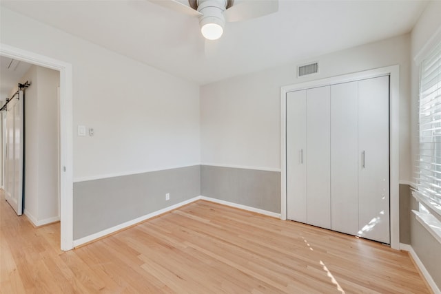 unfurnished bedroom with a barn door, ceiling fan, a closet, and light hardwood / wood-style floors