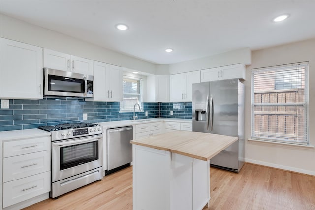 kitchen with appliances with stainless steel finishes, light wood-type flooring, sink, white cabinets, and a kitchen island