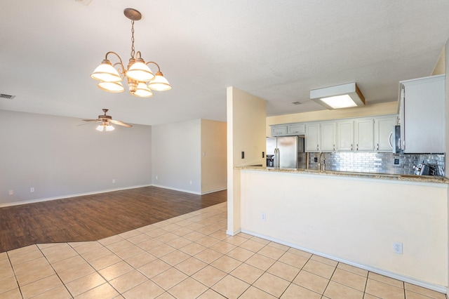 kitchen with decorative backsplash, ceiling fan with notable chandelier, stainless steel appliances, light tile patterned floors, and pendant lighting